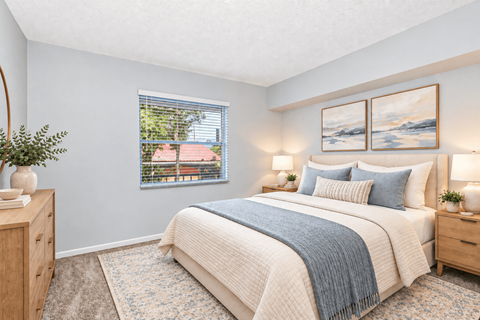 A bedroom with a large bed and a window showing a view of a red roof.