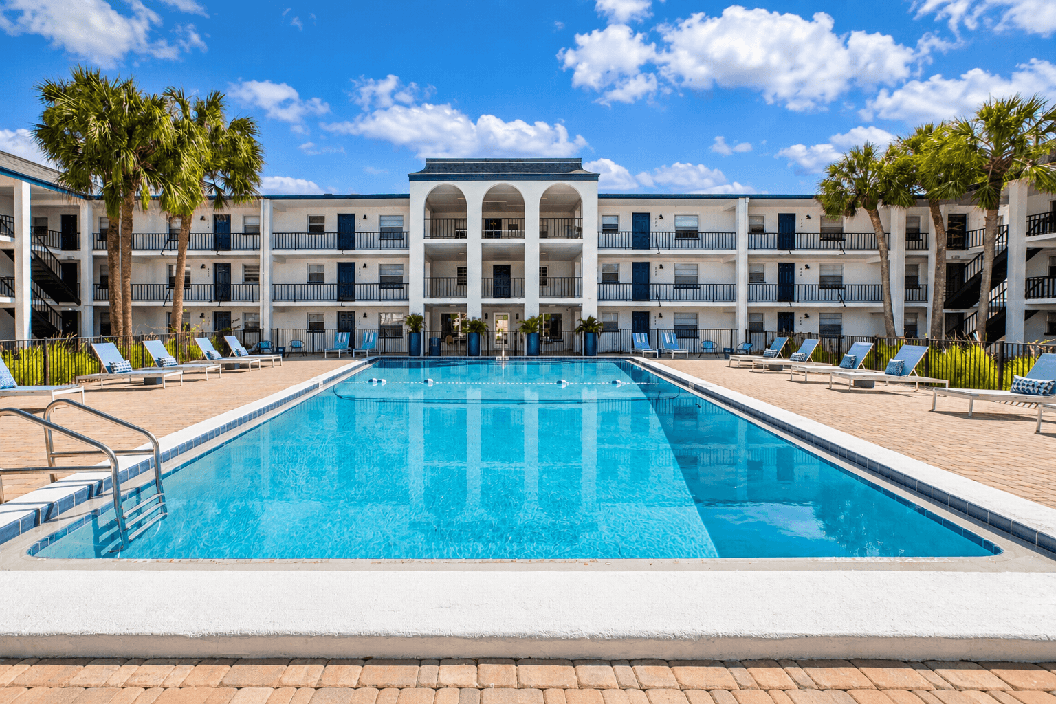 A large swimming pool in front of a building with palm trees.