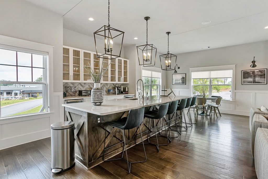 a kitchen with a long island with bar stools and chairs and two hanging lights