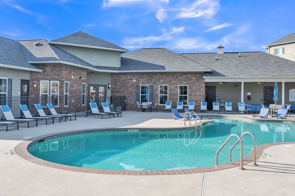 A swimming pool is surrounded by lounge chairs in front of a building.