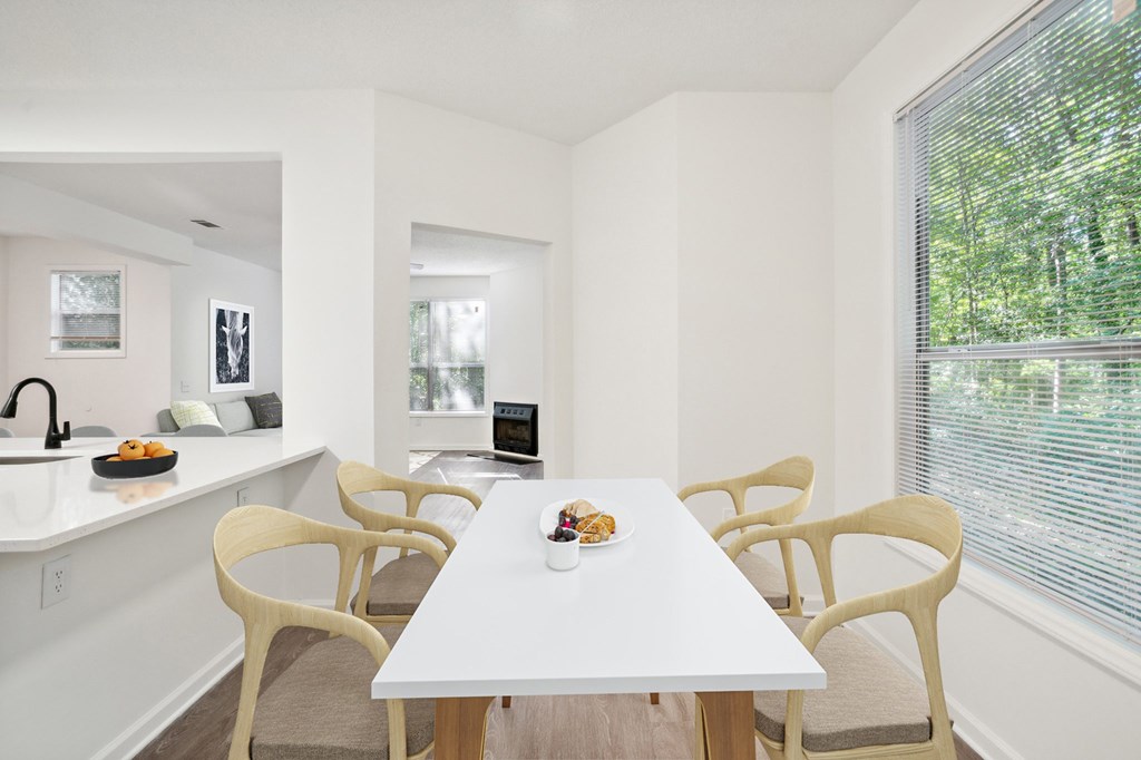 A white dining table with chairs and a bowl of fruit on it.