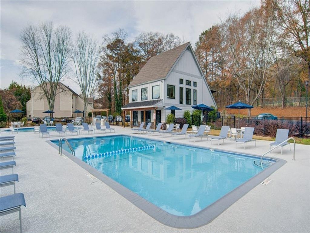 a swimming pool with chairs and a house in the background
