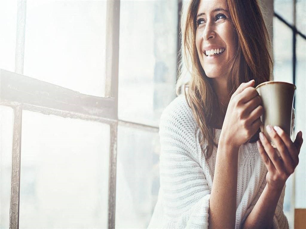 a woman smiling while holding a cup of coffee