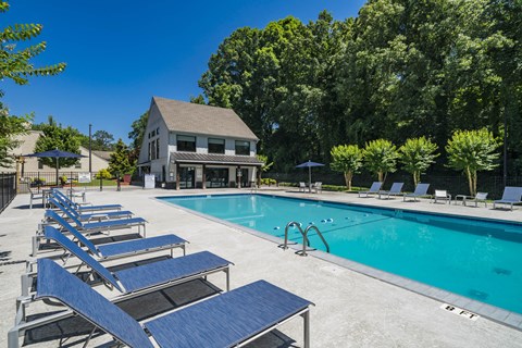 A pool with sun loungers and a building in the background.