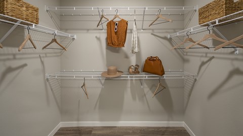 A white closet with clothes hanging on hangers.