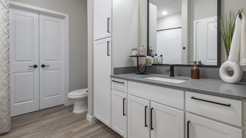 A bathroom with a white toilet, sink, and cabinets.