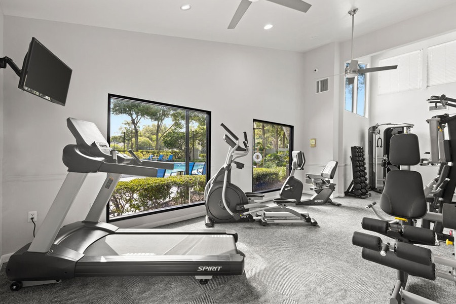 the gym has plenty of exercise equipment and a view of the pool