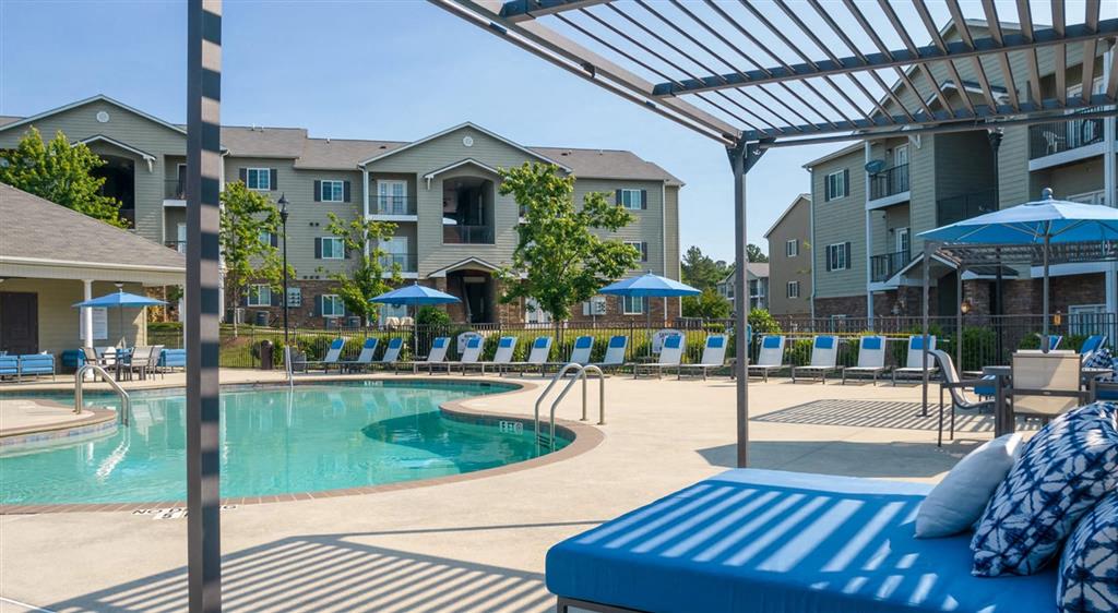 a pool with lounge chairs and umbrellas in front of apartment buildings