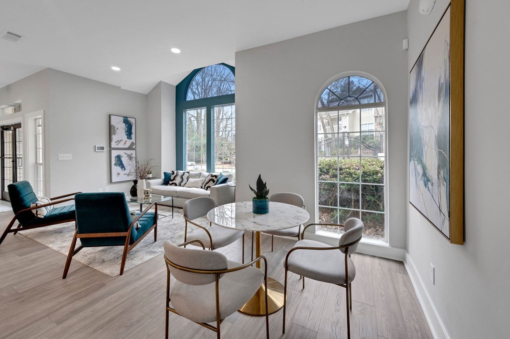 a living room with a round table and chairs and large windows