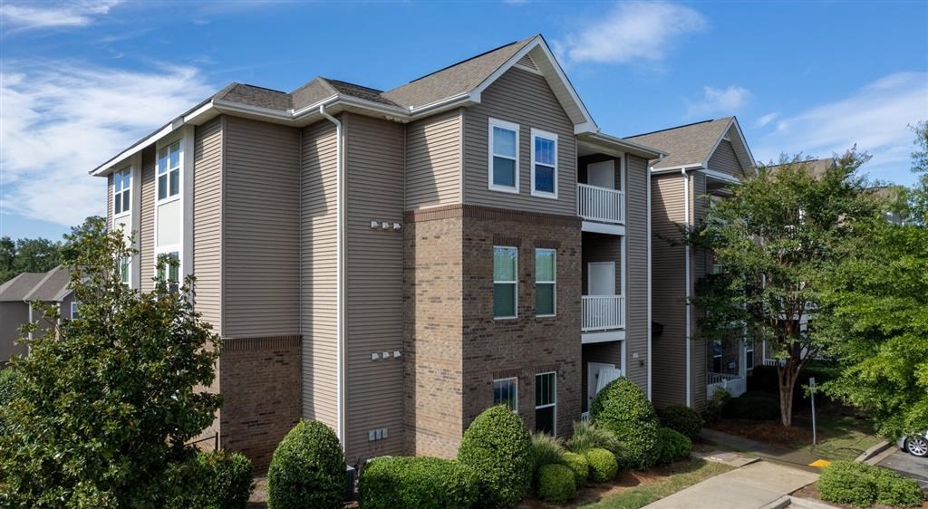 an apartment building with brown siding and trees and bushes