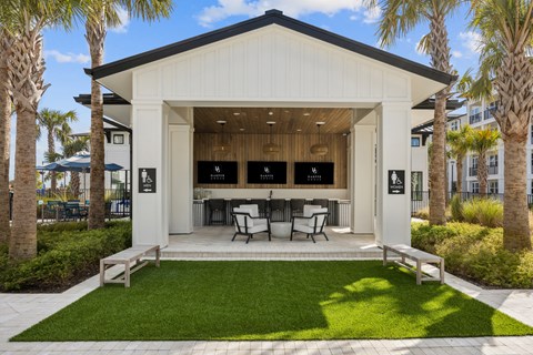A white building with a black roof and a glass door is surrounded by palm trees.
