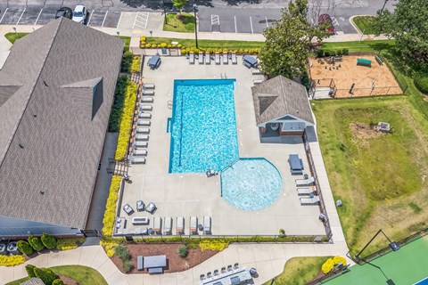 An aerial view of a swimming pool surrounded by a grassy area and a parking lot.