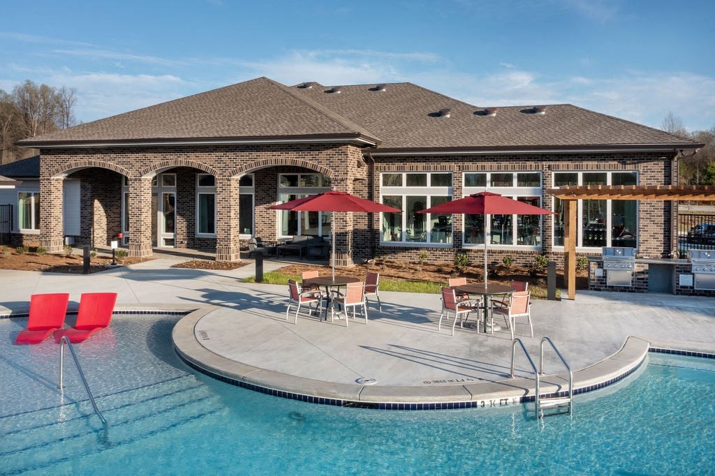 a swimming pool with chairs and umbrellas in front of a house