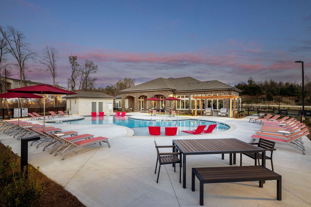 a swimming pool with chairs and tables around it at dusk