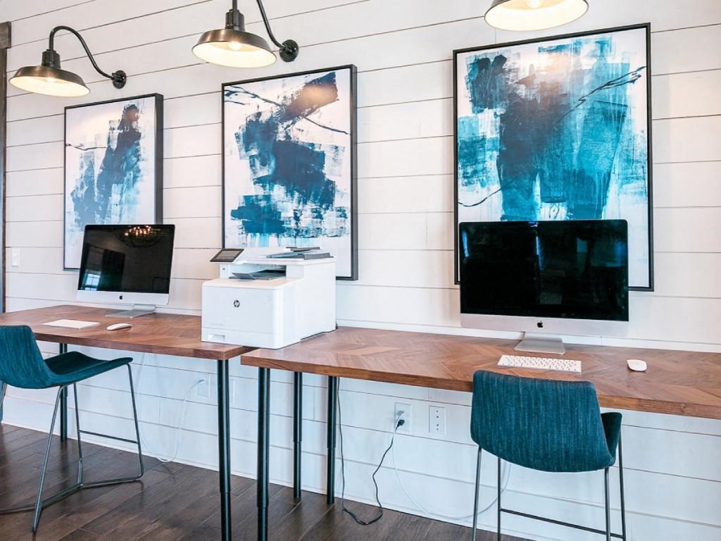 two computer monitors on a desk in a room with two chairs