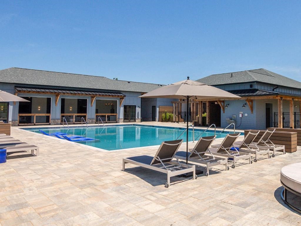 a swimming pool with chairs and an umbrella in front of a house