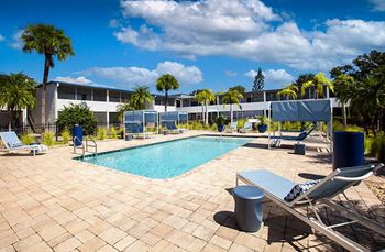 a swimming pool with chairs and a building in the background