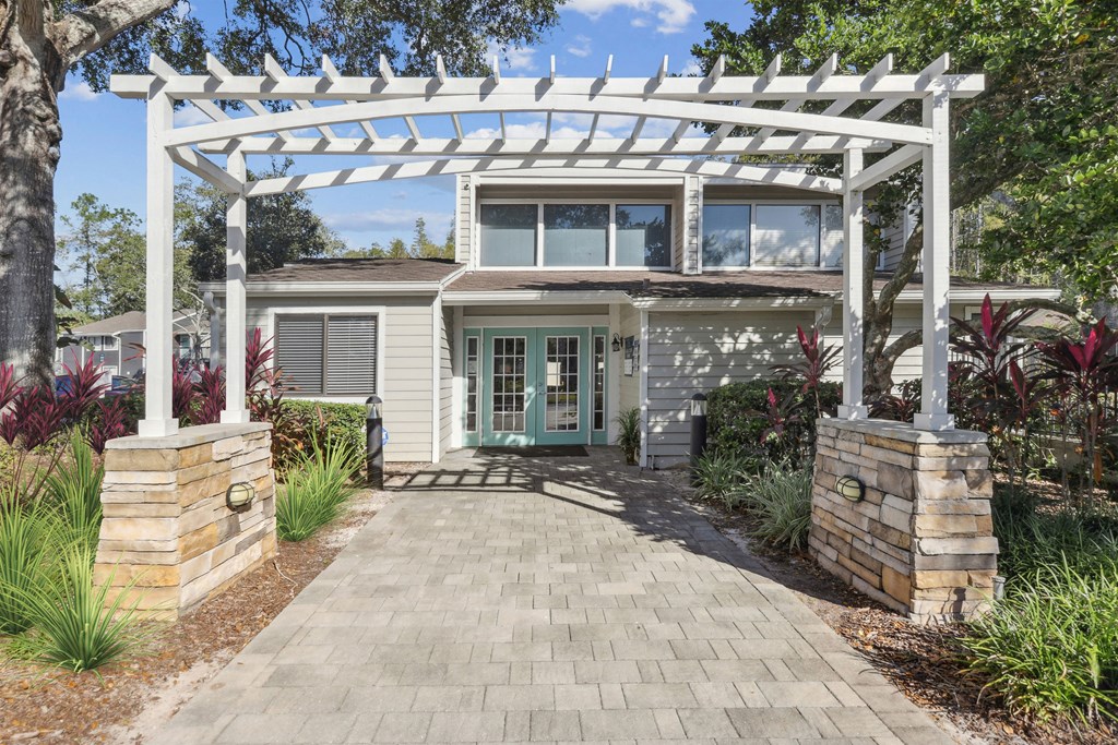 the front of a house with a white pergola and a brick pathway