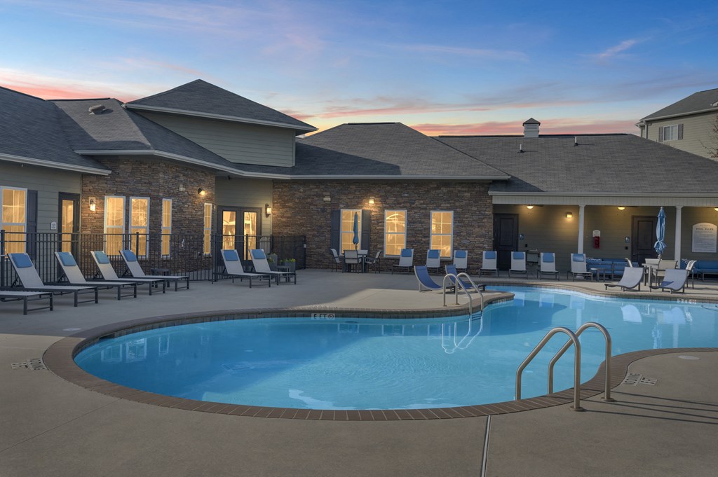A large outdoor swimming pool with lounge chairs and a building with a stone facade.