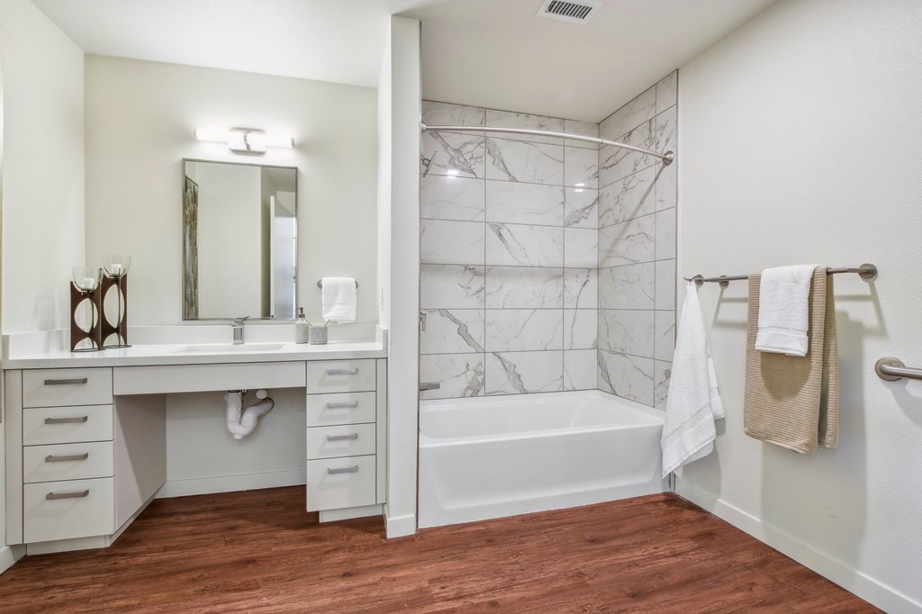 A white bathroom with a marble tile shower and a wooden floor.