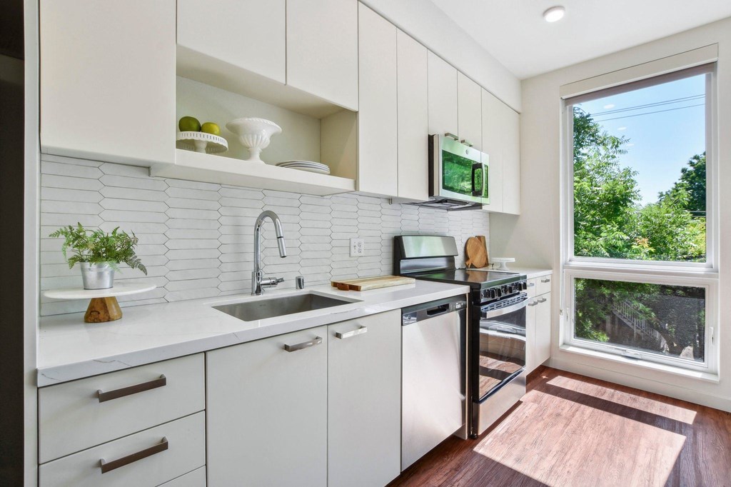A kitchen with white cabinets and a window overlooking a tree.