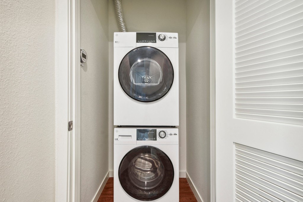 A white washing machine and dryer stacked on top of each other in a small room.