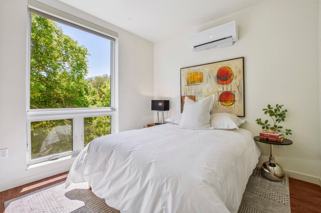 A bedroom with a large bed and a window overlooking trees.