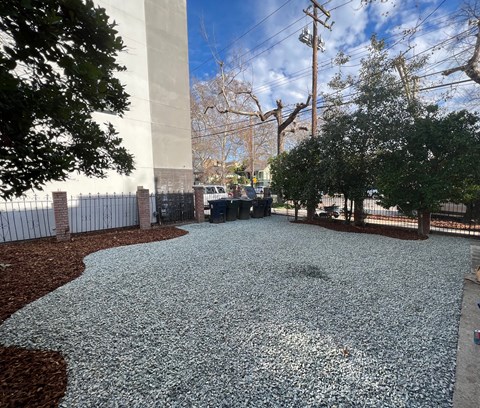 A gravel area with a fence and trees in the background.