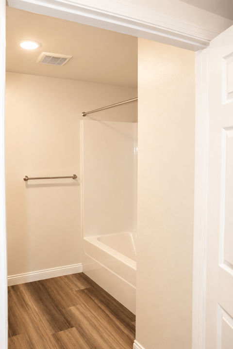 A white bathroom with a wooden floor and a white door.