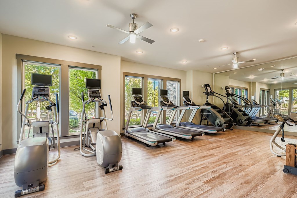 A spacious gym with a variety of equipment including treadmills, elliptical machines, and a fan.