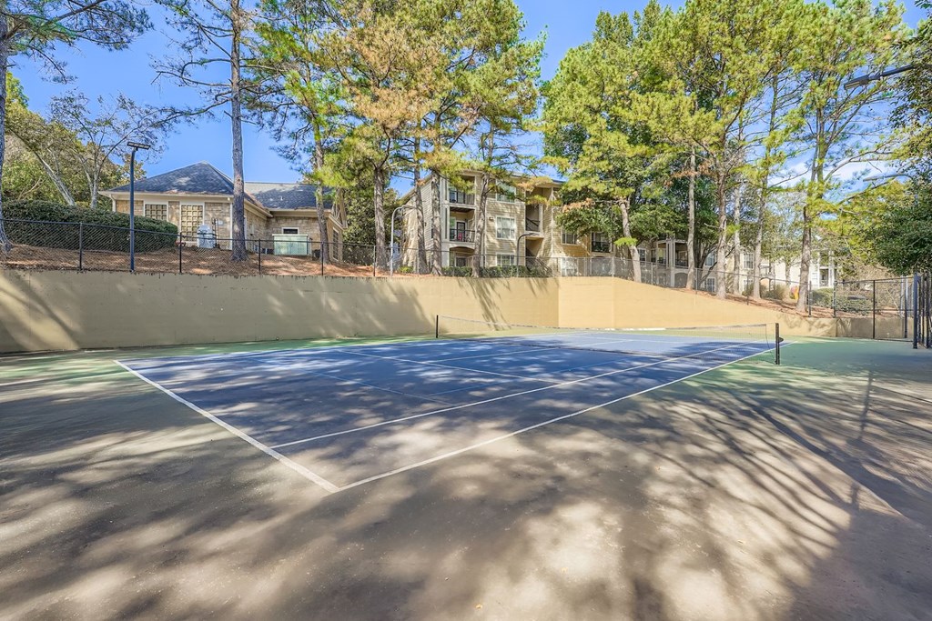 A tennis court surrounded by trees and apartment buildings.