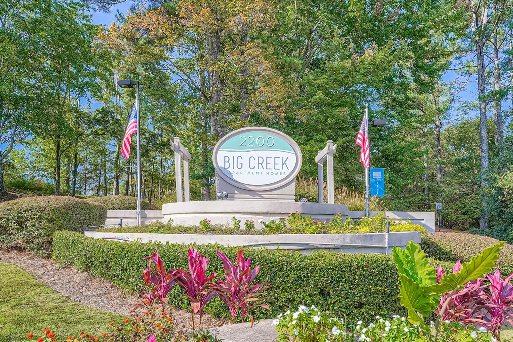 A sign for Big Creek stands in a garden with flowers and trees in the background.