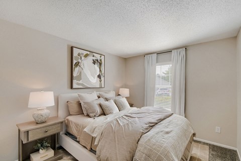 A bedroom with a bed, nightstand, and a painting on the wall.