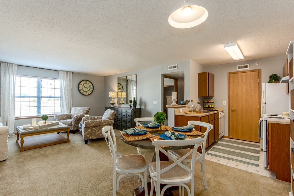 A well-lit, clean, and organized living room with a dining area and kitchen in the background.