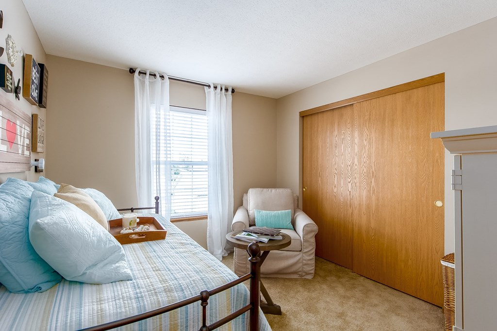 A bedroom with a bed, chair, and wooden door.