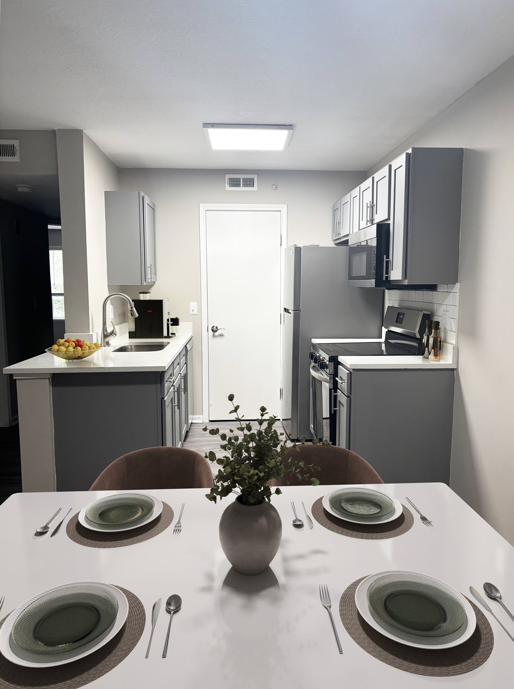 A dining table set with plates and cutlery is in the foreground of a modern kitchen.