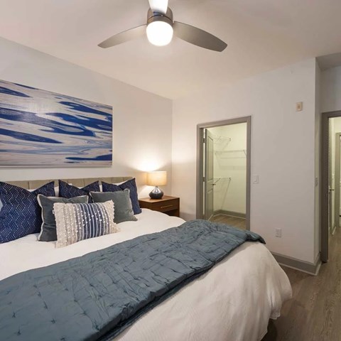 A bedroom with a bed, pillows, a ceiling fan, and a painting on the wall.