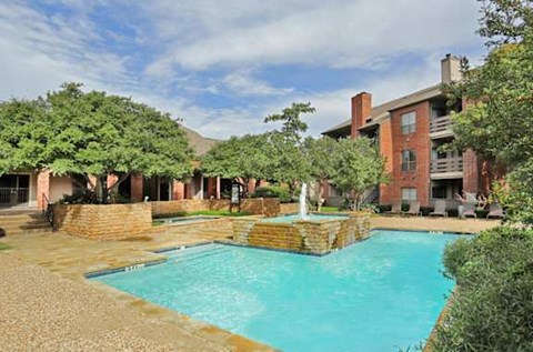 A large outdoor swimming pool surrounded by a brick wall and a fountain.