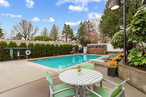 A table with a plant on it sits in front of a pool.