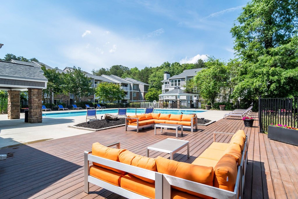 A wooden deck with orange cushions and a pool in the background.