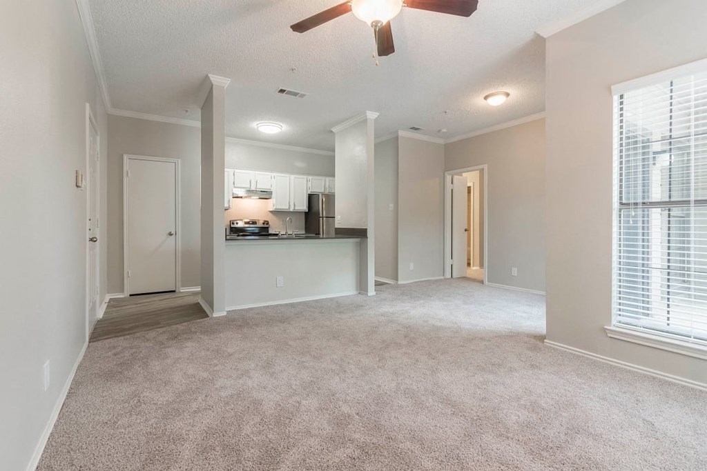A spacious living room with a carpeted floor and a ceiling fan.