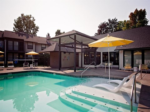 A pool with a yellow umbrella and white chairs.