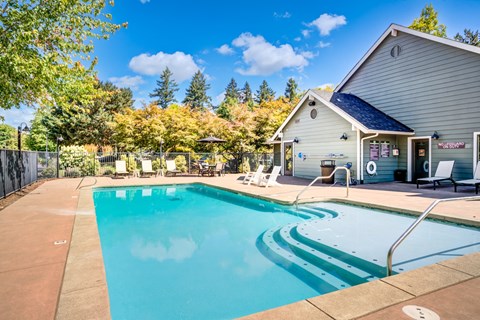 A swimming pool in front of a house with trees in the background.
