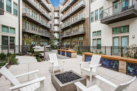 A patio area with white chairs and tables in front of apartment buildings.