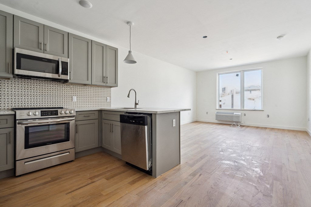 an empty kitchen with stainless steel appliances and a wooden floor