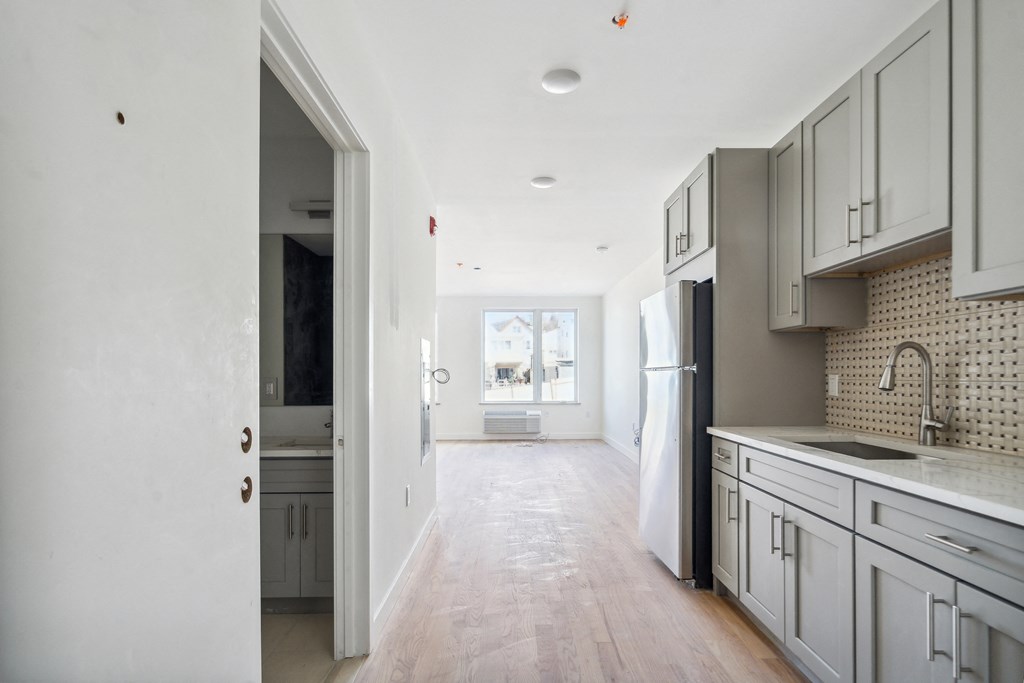 a renovated kitchen with white cabinets and white appliances and a hallway to the living room