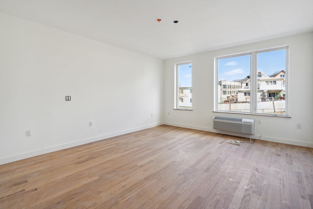 the living room of an apartment with wood flooring and large windows