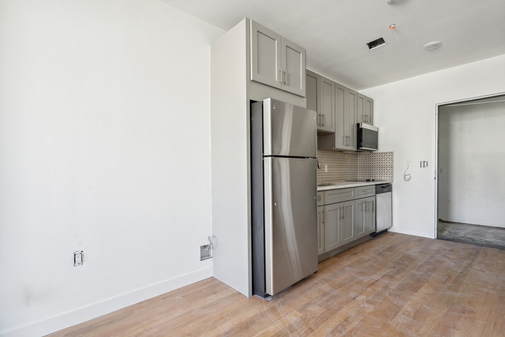 an empty living room with a refrigerator and a kitchen
