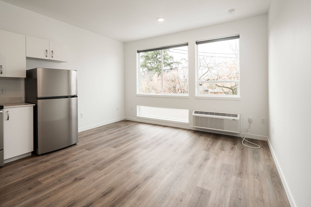 an empty living room with a refrigerator and a window