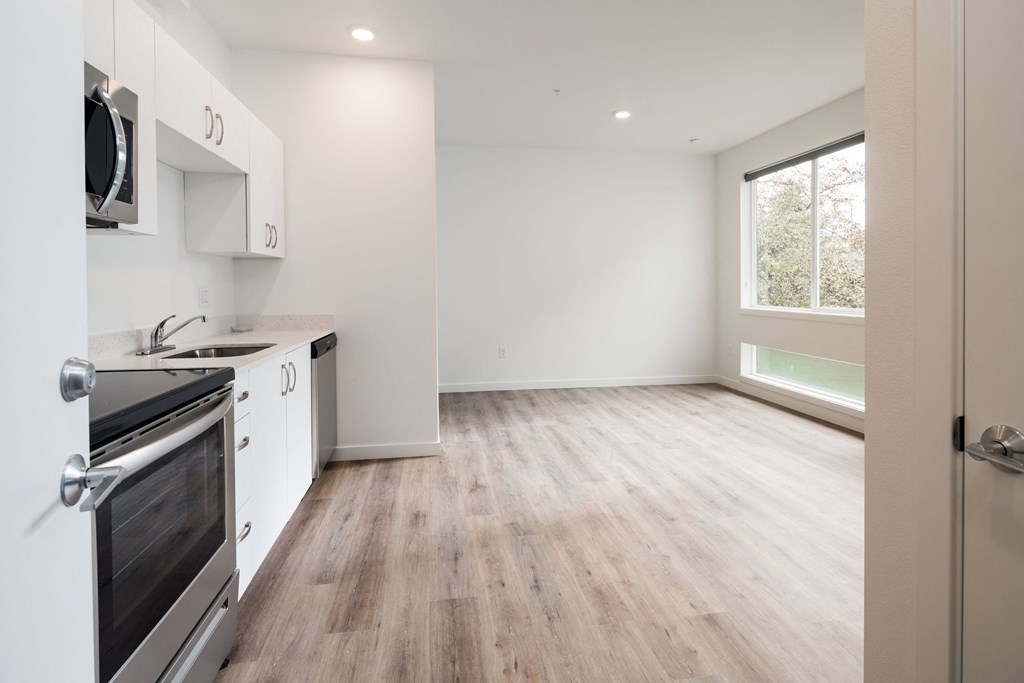 an empty kitchen and living room with white cabinets and a window